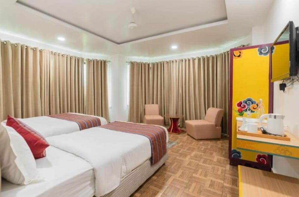 A cozy hotel room features twin beds with colorful throws, beige curtains, vibrant yellow decor, and a warm ambiance, ideal for travelers seeking comfort and cultural charm.