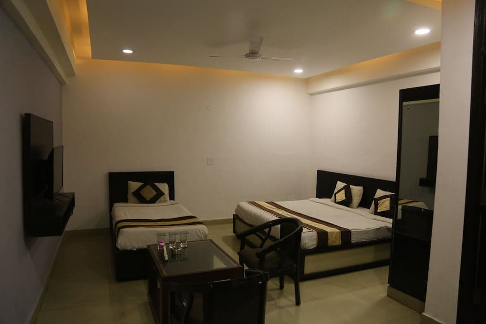 A cozy hotel room features two neatly made beds, a small dining table with chairs, a wall-mounted TV, and soft ambient lighting, ideal for travelers seeking comfort and relaxation.