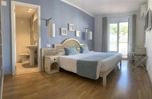 A cozy hotel room with a neatly made bed, blue walls, wooden flooring, and an open bathroom, exudes a serene and inviting atmosphere perfect for travelers seeking relaxation.