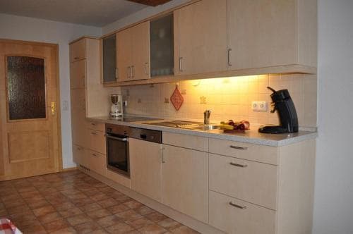 A cozy kitchen with beige cabinets, tiled flooring, and warm lighting creates an inviting atmosphere, perfect for travelers seeking a homey rental space equipped with essential appliances like a stove and coffee maker.