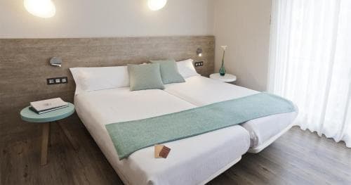 A cozy hotel room features a neatly made bed with teal accents, wooden bedside tables, and soft lighting, creating a serene atmosphere ideal for relaxation during a travel getaway.
