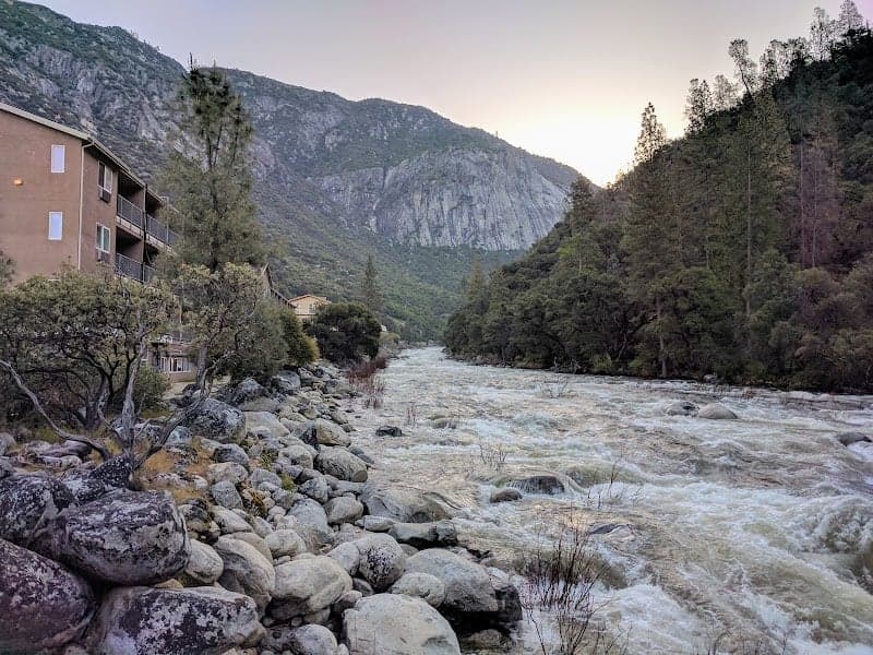 A serene riverside lodge nestled among rocky banks and towering mountains offers a tranquil retreat for nature enthusiasts seeking adventure in El Portal, California.