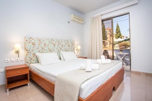 A cozy hotel room with a neatly made bed, wooden nightstands, and a view of a serene outdoor patio through glass doors, ideal for travelers seeking relaxation and comfort.