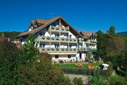 A charming alpine hotel with balconies adorned by flower boxes stands amidst lush greenery under a clear blue sky, ideal for travelers seeking a serene mountain retreat.