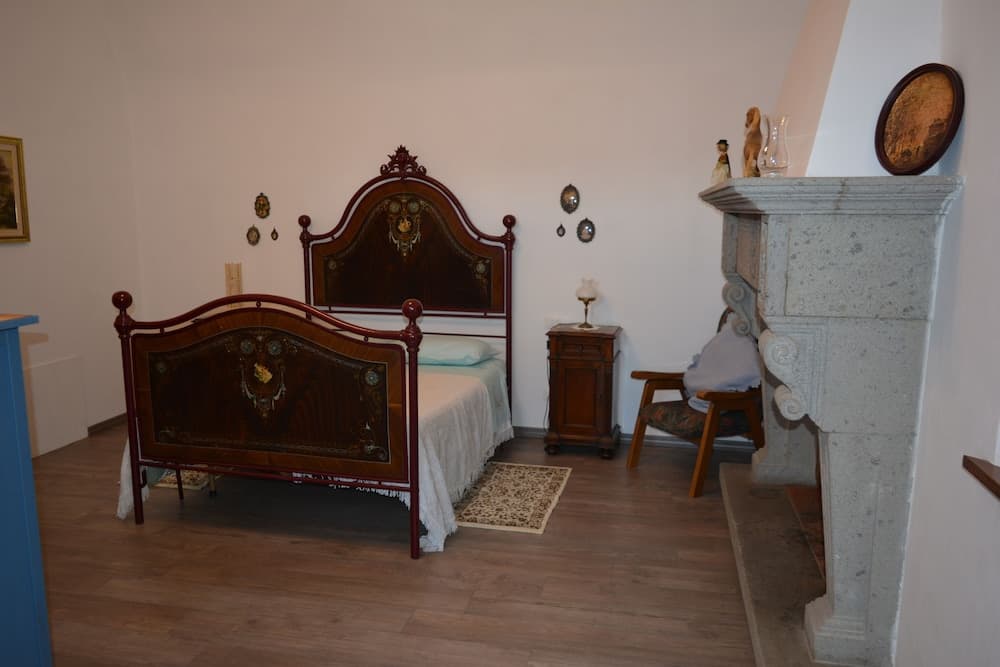 A cozy bedroom with vintage wooden furniture, a stone fireplace adorned with decorative items, and soft lighting creates an inviting atmosphere ideal for travelers seeking a charming and historical accommodation experience.
