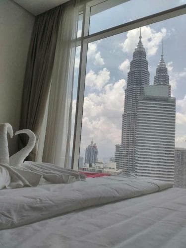 A cozy hotel room with swan-shaped pillows overlooks the iconic Petronas Twin Towers under a partly cloudy sky, ideal for travelers seeking urban views and comfort.
