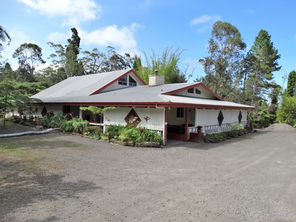 A serene rural retreat features a charming white house with red trim surrounded by lush greenery under a bright blue sky, ideal for travelers seeking a peaceful countryside escape.