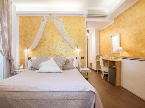 A cozy hotel room features a bed adorned with a delicate canopy against warm yellow walls, complemented by wooden furnishings and soft lighting, ideal for travelers seeking comfort and relaxation.