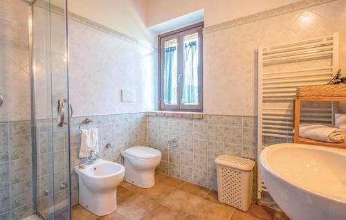 A cozy hotel bathroom features tiled walls, a walk-in shower, a bidet, a toilet, a sink, and a window letting in natural light, ideal for travelers seeking comfort and cleanliness.