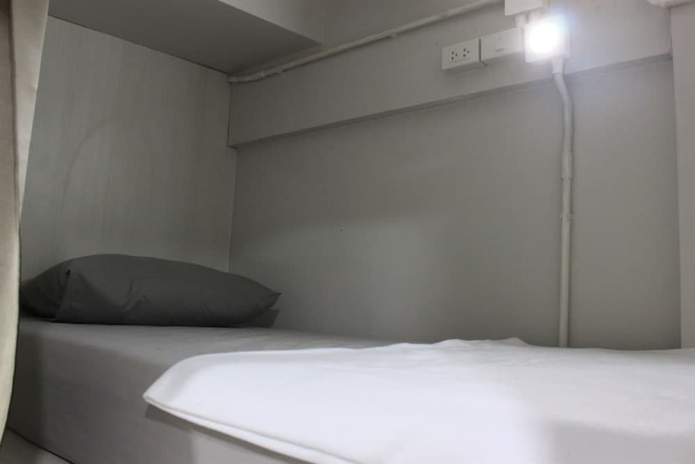 A cozy, minimalist bunk bed with white linens and a gray pillow in a compact hostel room, ideal for budget travelers seeking simple accommodations.