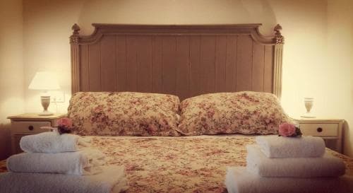 A cozy bedroom with a floral-patterned bedspread, wooden headboard, and neatly folded towels exudes warmth and comfort, ideal for travelers seeking a serene and inviting accommodation.