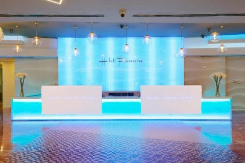A modern hotel lobby exudes elegance with its sleek reception desk, glowing blue backdrop, and warm pendant lights, ideal for travelers seeking luxury accommodations.