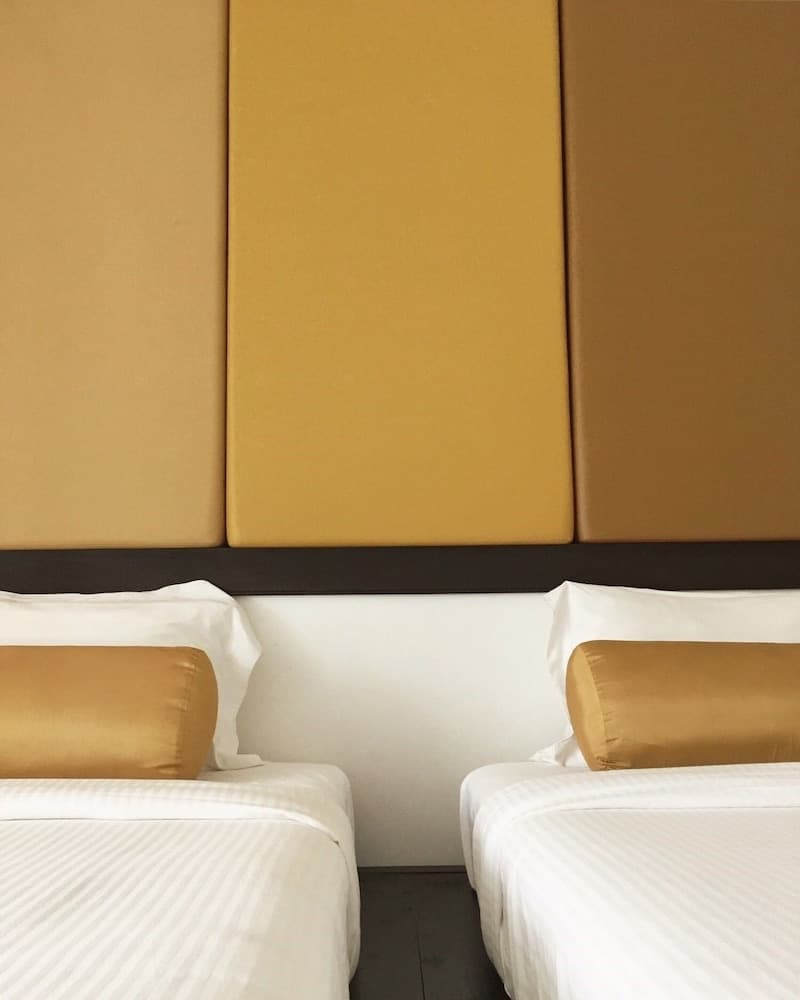 A cozy hotel room features two neatly made beds with white linens and mustard-yellow pillows against a modern, color-blocked wall, ideal for travelers seeking comfort and style.