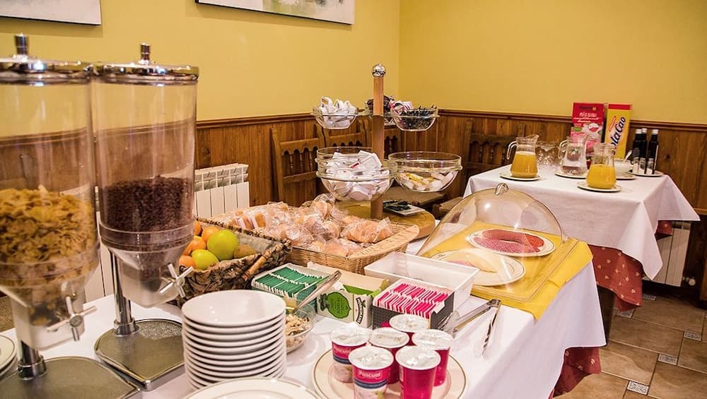 A cozy indoor breakfast buffet scene features an inviting array of cereals, fresh fruits, pastries, and beverages on neatly arranged tables, perfect for travelers seeking a hearty morning meal in a warm and welcoming atmosphere.