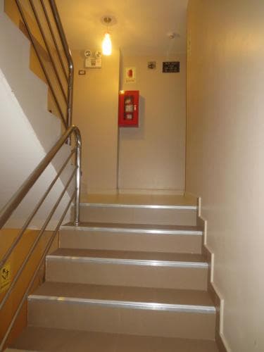 A well-lit indoor staircase with beige steps and metal railings leads up to a hallway featuring a fire alarm box, ideal for travelers seeking accessible accommodations in urban settings.