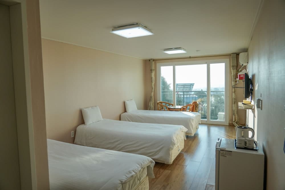 A cozy hotel room with three neatly arranged beds, wooden flooring, a balcony view of greenery, and modern amenities creates a serene atmosphere ideal for travelers seeking comfort and relaxation.