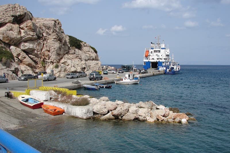 A serene coastal harbor scene in Kamiros Skala, Greece, features a ferry docked near small boats, surrounded by rugged cliffs and calm waters, ideal for travelers seeking a tranquil seaside getaway.