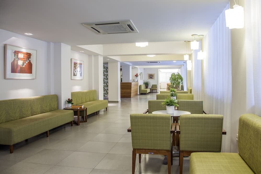 A serene hotel lobby features modern green seating, white curtains, and artwork, creating a welcoming atmosphere ideal for travelers seeking relaxation and comfort.