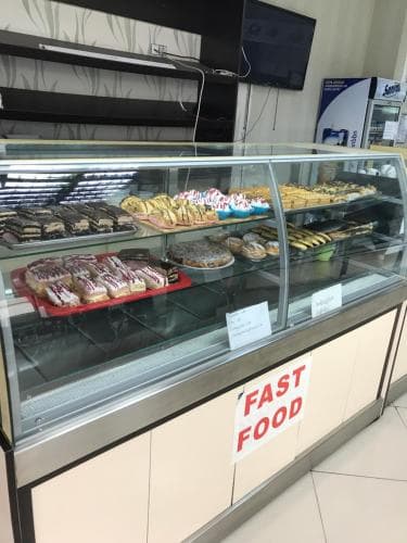 A brightly lit bakery display case filled with assorted pastries and desserts invites travelers to indulge in quick treats at an airport or transit hub.
