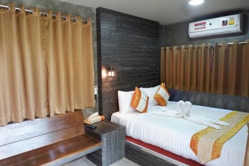A cozy hotel room features a neatly made bed with orange accents, wooden furnishings, and warm curtains, creating a welcoming atmosphere ideal for travelers seeking comfort and relaxation.