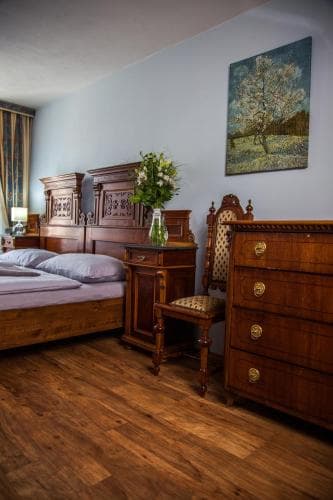 A cozy hotel bedroom features antique wooden furniture, a vibrant floral arrangement, and a Van Gogh-inspired painting, creating an inviting atmosphere ideal for travelers seeking a charming and artistic retreat.