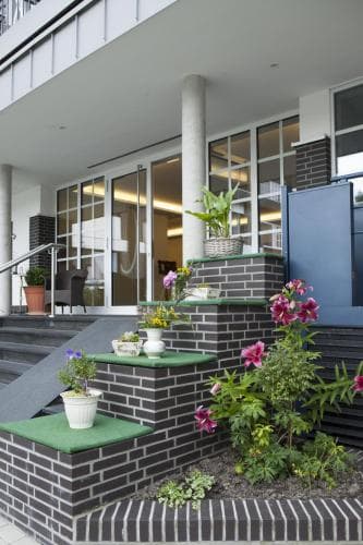 A welcoming urban apartment entrance features a charming brick staircase adorned with vibrant flowers and greenery, creating an inviting atmosphere ideal for city travelers seeking a cozy retreat.