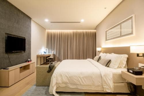 A cozy modern hotel room features a neatly made bed, soft lighting, a sleek desk setup, and a mounted TV, ideal for travelers seeking comfort and functionality during their stay.