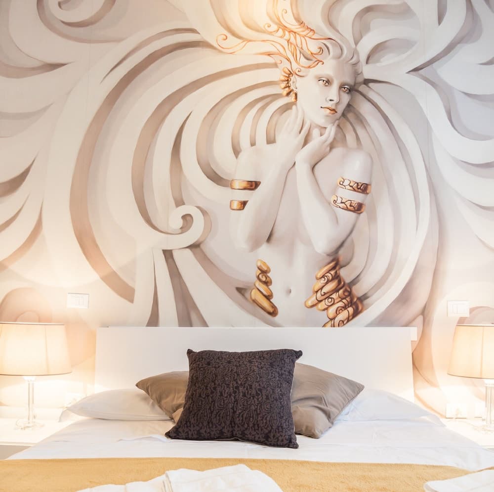 A luxurious hotel room features an ornate mural of a classical figure adorned with gold accents, creating an elegant and artistic atmosphere ideal for travelers seeking a unique and sophisticated stay.