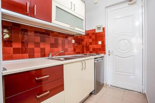 A cozy apartment kitchen with vibrant red tiles and cabinetry exudes warmth and functionality, ideal for travelers seeking a homey cooking space during their stay.