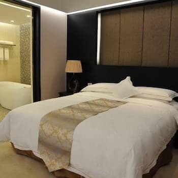 A cozy hotel room features a neatly made bed with plush pillows, a stylish bedside lamp, and an adjacent bathroom with a bathtub, ideal for travelers seeking comfort and relaxation.
