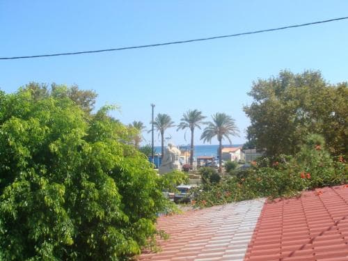 A serene coastal village scene with vibrant greenery, palm trees, a statue, and red-tiled rooftops under a clear blue sky, ideal for travelers seeking a tranquil seaside retreat.