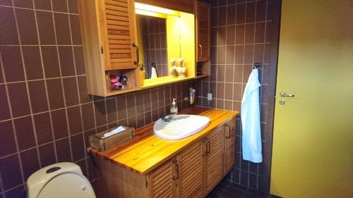 A cozy bathroom with wooden cabinetry, tiled walls, and a warm yellow door creates an inviting atmosphere, perfect for travelers seeking comfort in compact spaces.