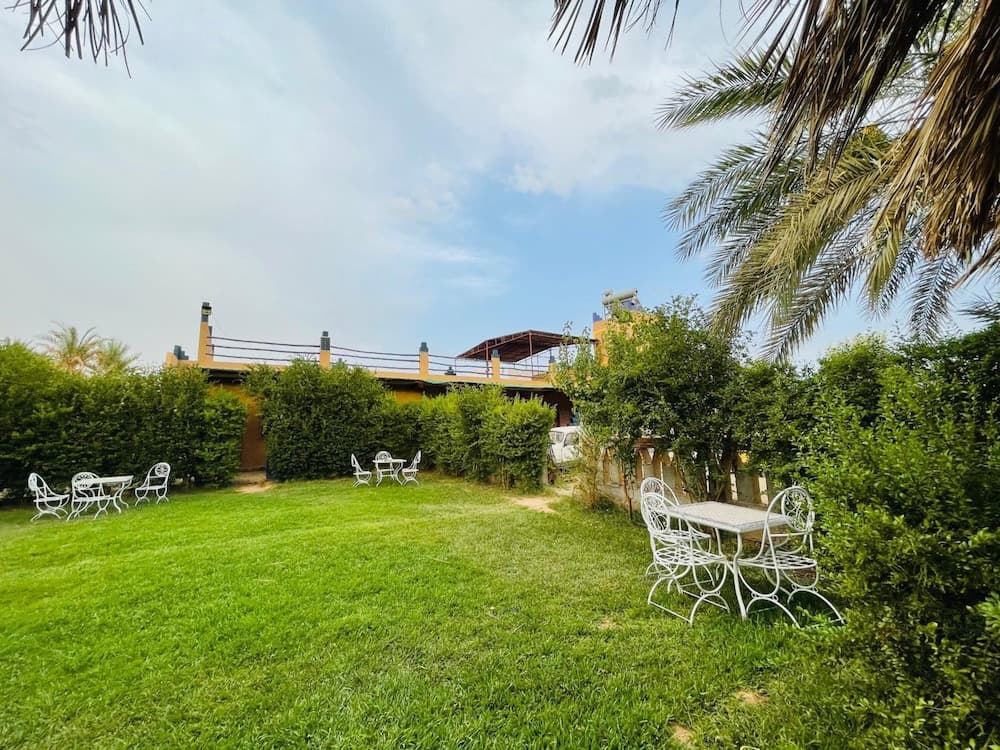 A serene garden with lush green grass, white patio furniture, and palm trees frames a tranquil outdoor space ideal for relaxation and leisurely stays.