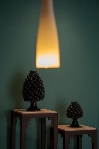 A cozy indoor setting features two pinecone sculptures on wooden pedestals under the warm glow of a hanging lamp, ideal for travelers seeking unique decor inspiration or photography backdrops.