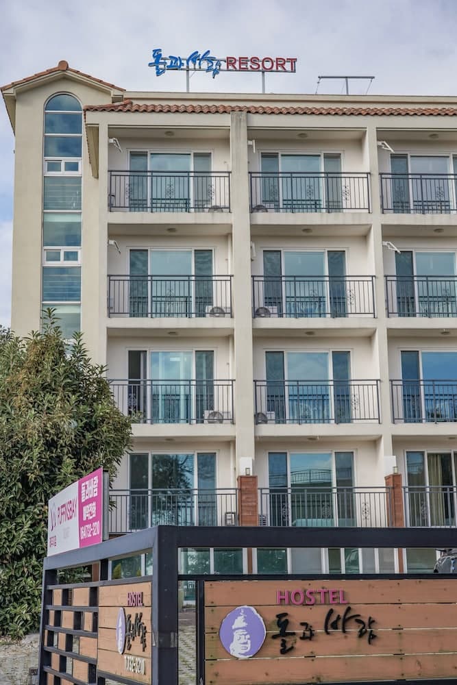 A serene resort building with balconies and a welcoming hostel sign offers travelers a cozy retreat in a tranquil setting, ideal for vacation planning and accommodation searches.