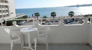 A serene coastal balcony offers a picturesque view of the sea and palm trees, featuring white furniture perfect for relaxing getaways or romantic retreats.