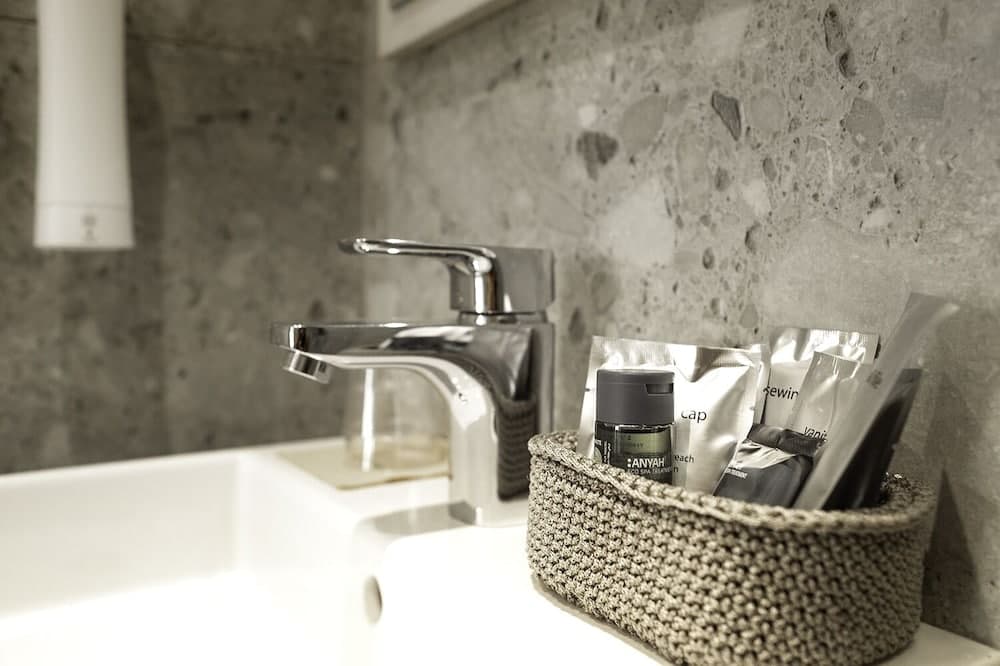 A modern bathroom sink with a sleek faucet and textured stone wall exudes a minimalist mood, featuring neatly arranged toiletries in a woven basket, ideal for travelers seeking clean and stylish accommodations.