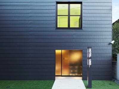 A modern hotel entrance with sleek black siding, glowing warm interior lights, and a minimalist signboard creates an inviting urban retreat ideal for travelers seeking contemporary accommodations.