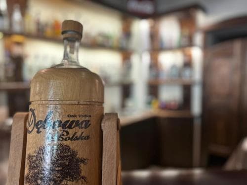 A cozy bar ambiance features a wooden bottle of Żubrówka vodka in focus, ideal for travelers seeking unique spirits and cultural experiences.