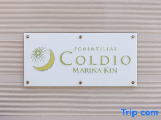 A serene signboard for "Pool & Villas Coldio Marina Kin" set against a textured beige wall, inviting travelers to explore luxurious accommodations near a marina, ideal for vacation planning on Trip.com.