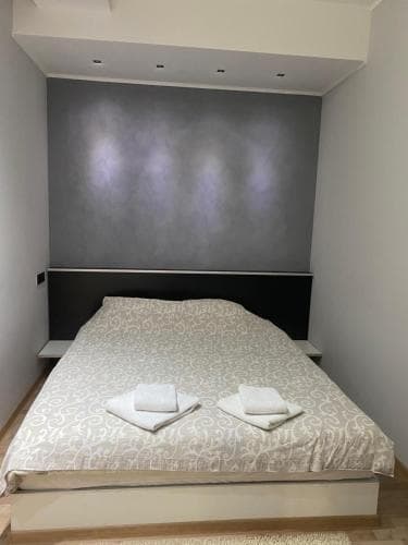 A cozy bedroom with a neatly made bed adorned with patterned bedding and folded towels, set against a sleek gray wall, ideal for travelers seeking a minimalist and tranquil accommodation experience.