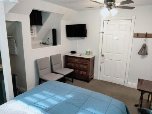 A cozy attic bedroom with slanted ceilings, a neatly made bed, wooden dresser, and mounted TV creates a warm and inviting atmosphere, ideal for travelers seeking a comfortable and private retreat.
