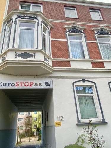 A charming European urban street scene featuring a historic brick building with ornate balconies, a EuroSTOPas bus stop sign, and a quiet residential atmosphere, ideal for travelers exploring city architecture and public transportation options.