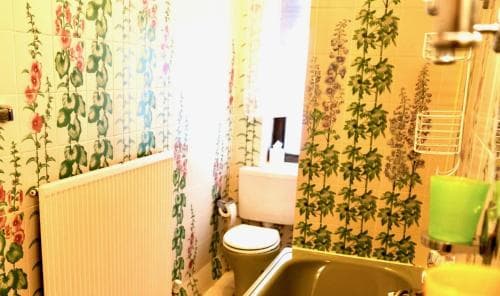 A cozy, vintage bathroom with floral wallpaper and yellow fixtures exudes a nostalgic charm, perfect for travelers seeking unique accommodations with retro aesthetics.