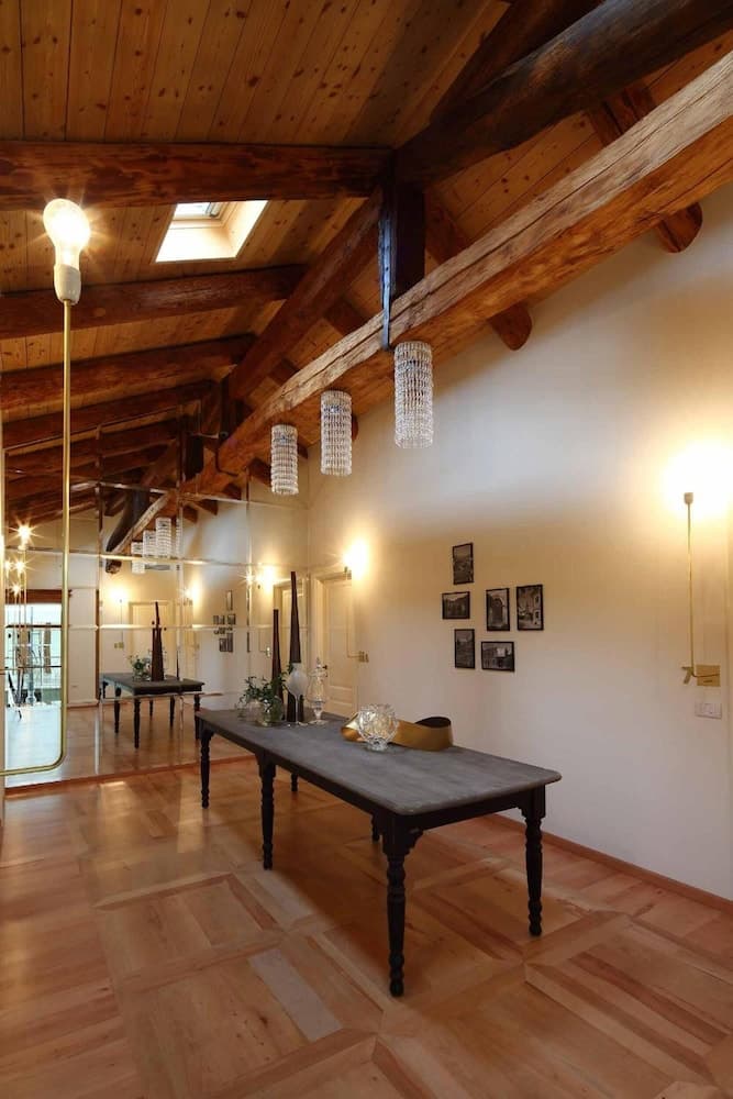A cozy rustic dining room with wooden beams, parquet flooring, elegant chandeliers, and a long table adorned with decorative items, ideal for travelers seeking a charming countryside retreat ambiance.