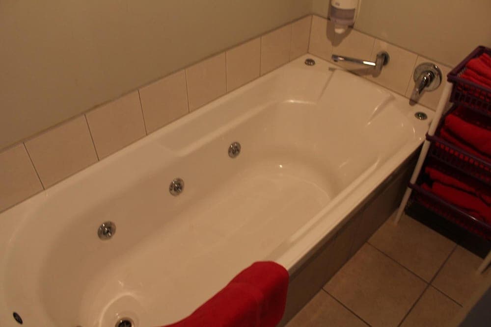 A cozy hotel bathroom features a white whirlpool bathtub with tiled walls, red towels neatly arranged in a basket, and a warm ambiance ideal for relaxation and rejuvenation.