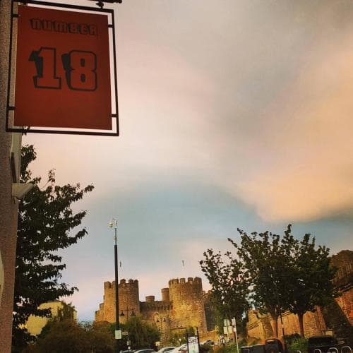 A picturesque evening view of a historic castle framed by lush trees, with a vibrant "Number 18" sign in the foreground, evokes a serene and nostalgic mood ideal for cultural heritage tourism.