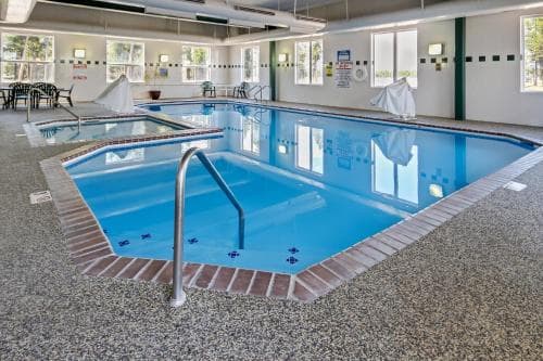 A serene indoor swimming pool area with clear blue water, surrounded by lounge chairs and large windows, offers a relaxing retreat for travelers seeking leisure and fitness activities.