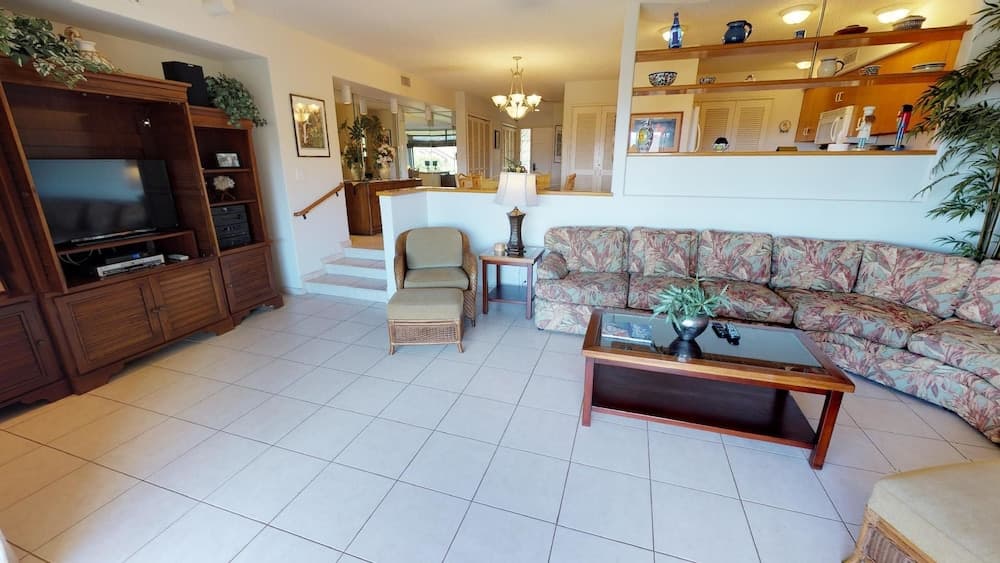 A cozy living room with tiled floors, floral-patterned furniture, and a wooden entertainment center creates a welcoming atmosphere ideal for vacation rentals or family stays.