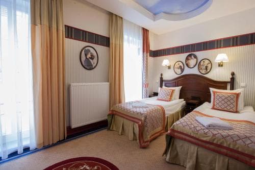 A cozy hotel room features twin beds adorned with patterned bedding, framed wall art, and soft lighting, creating an inviting atmosphere ideal for travelers seeking comfort and relaxation.